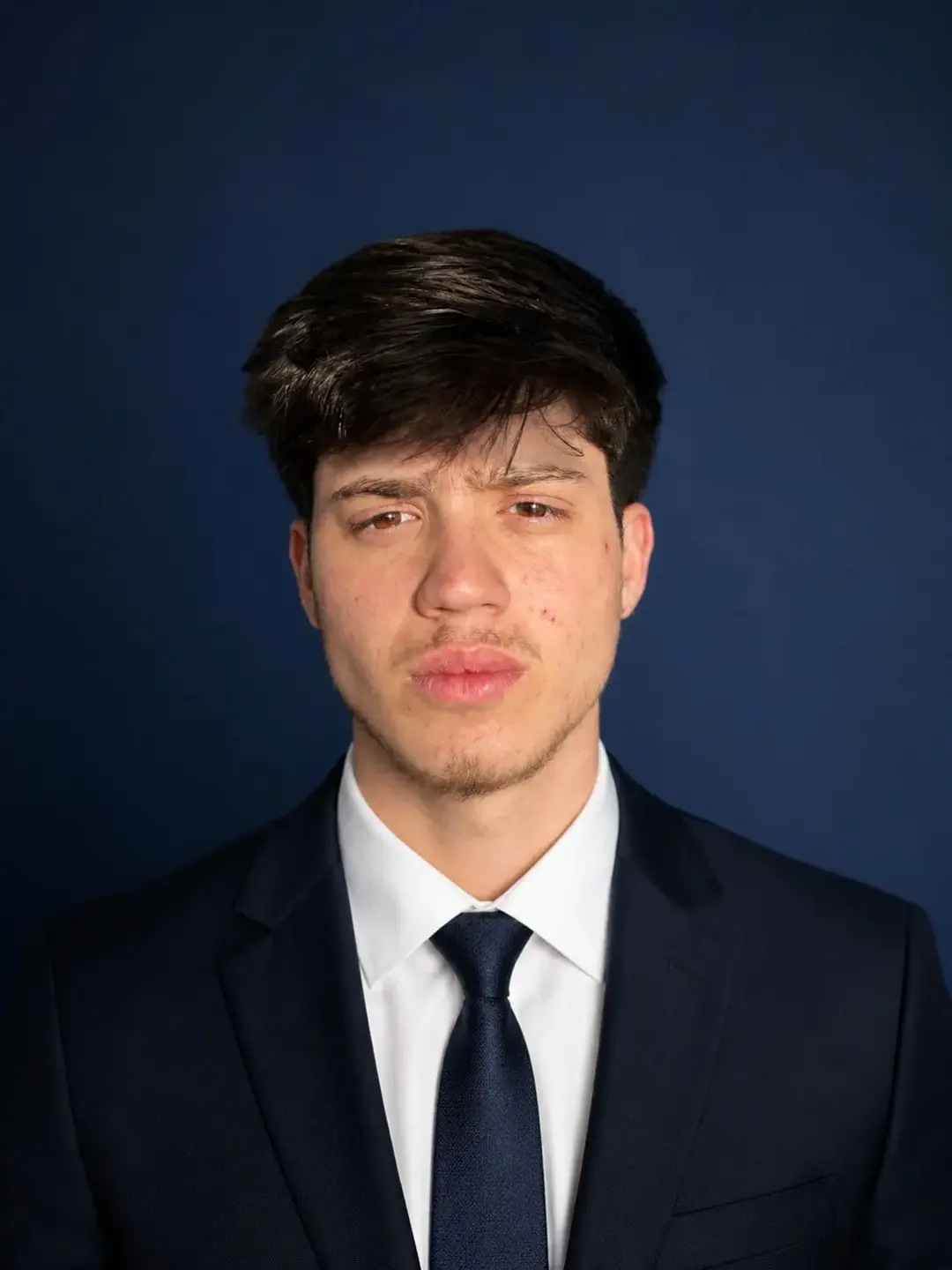 A professional portrait of Daniel, a co-founder of Ares Moving, in a corporate yet approachable setting. He is wearing a clean, branded polo shirt and smiling confidently. The lighting is professional studio quality with a soft blurred office background that maintains the company's minimalist corporate aesthetic.